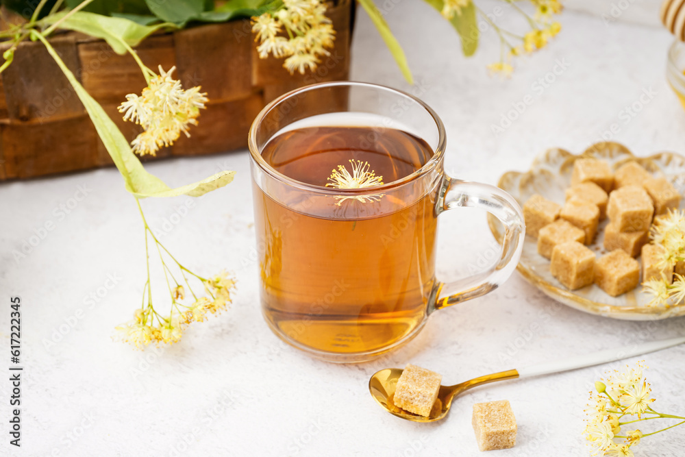 Glass cup of linden tea and plate with sugar on white background