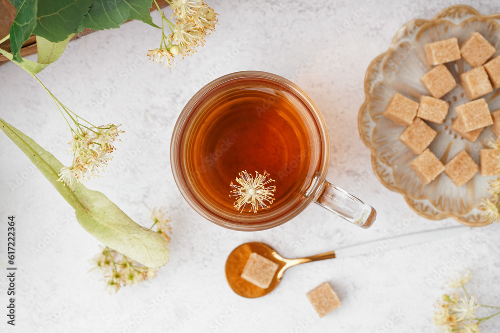 Glass cup of linden tea and plate with sugar on white background