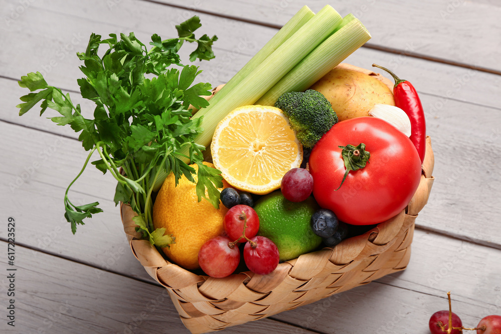 Wicker basket with different fresh fruits and vegetables on grey wooden background