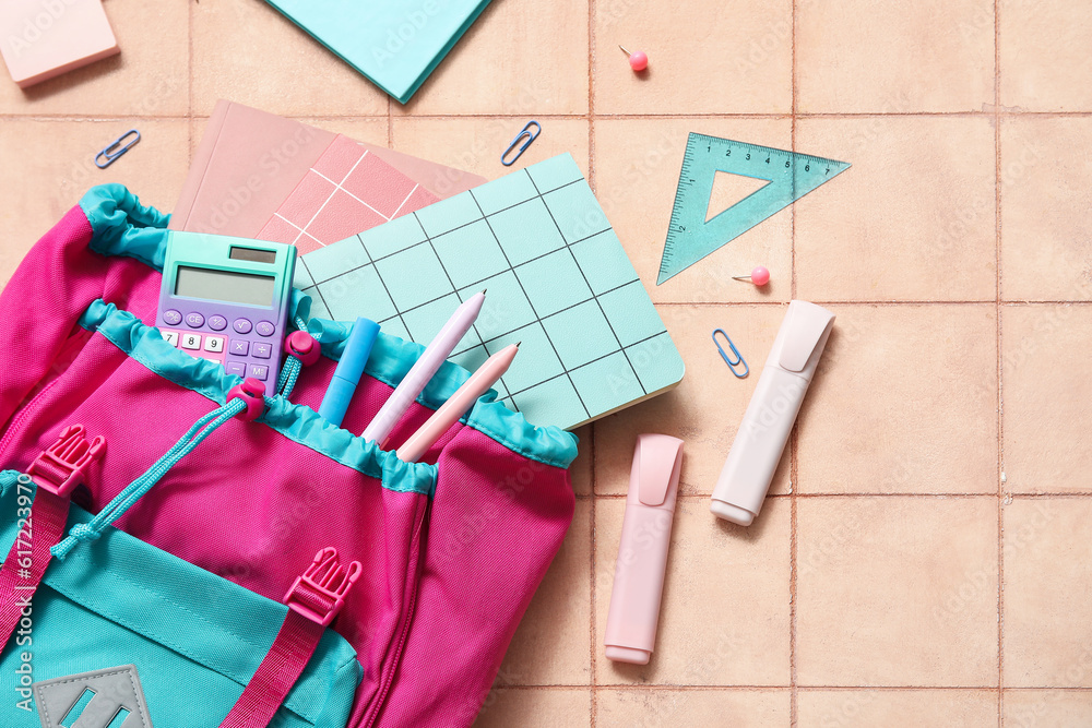 Colorful school backpack with notebooks, calculator and markers on beige tile background