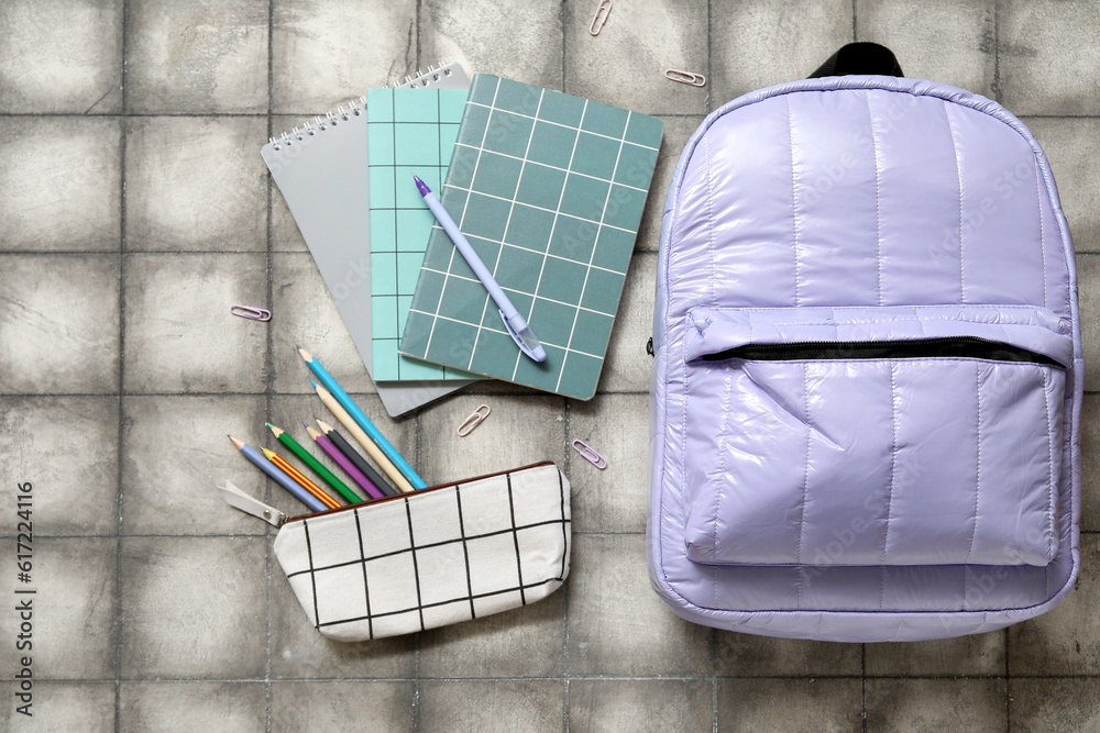 Lilac school backpack with notebooks, pencil case and paper clips on grey tile background