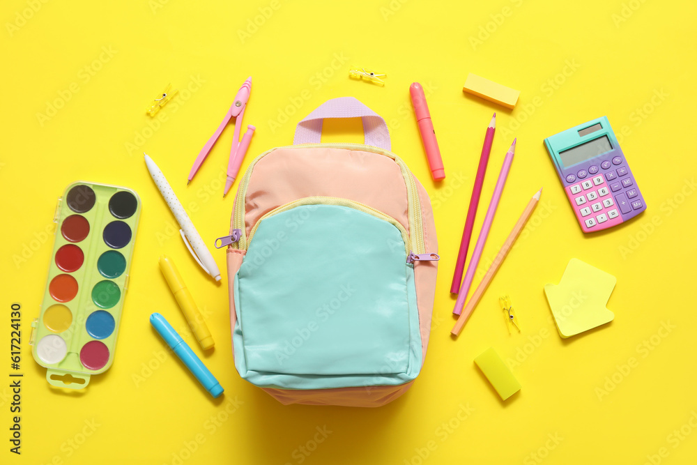 Colorful school backpack with watercolors, calculator and pencils on yellow background