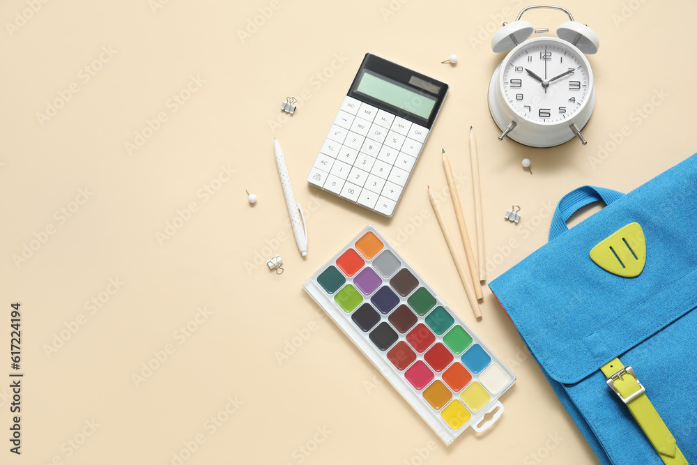 Blue school backpack with alarm clock, watercolors and calculator on beige background