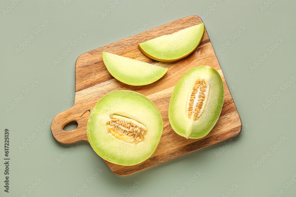 Wooden board with half of sweet melon and pieces on grey background