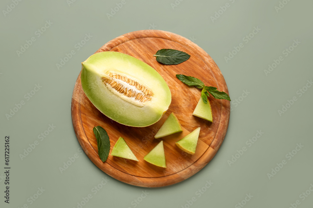 Wooden board with pieces of sweet melon and mint on grey background