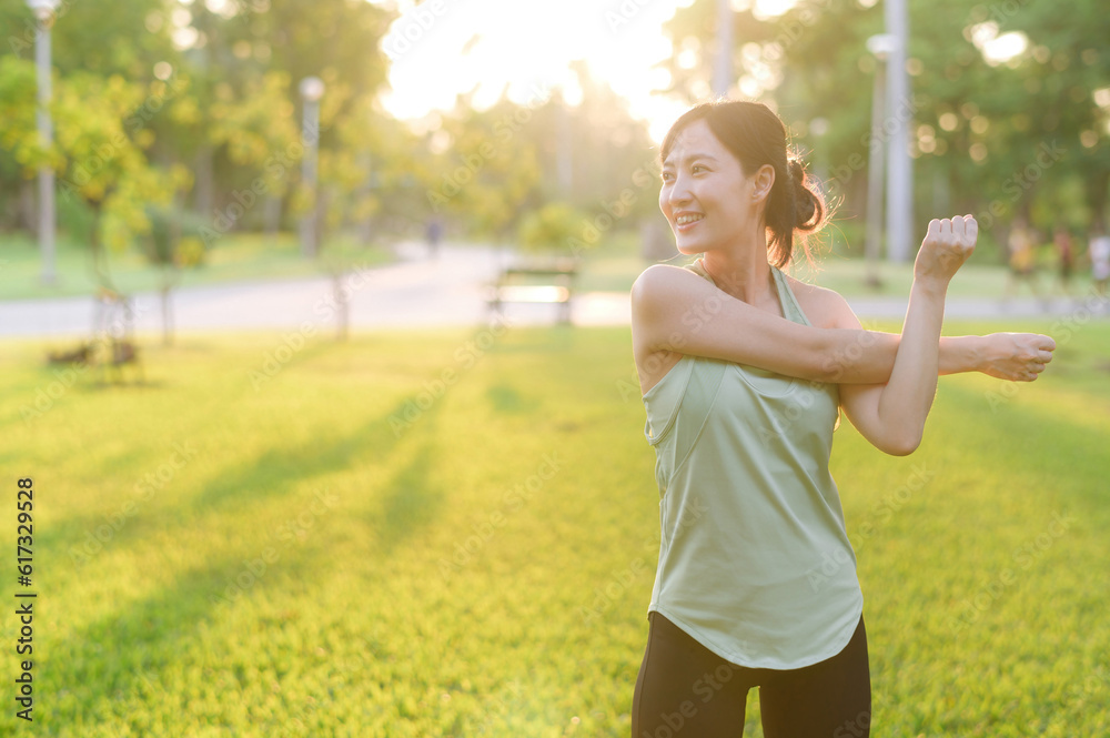 Female jogger. Fit young Asian woman with green sportswear stretching muscle in park before running 