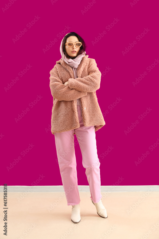 Stylish young woman in teddy coat and sunglasses near pink wall