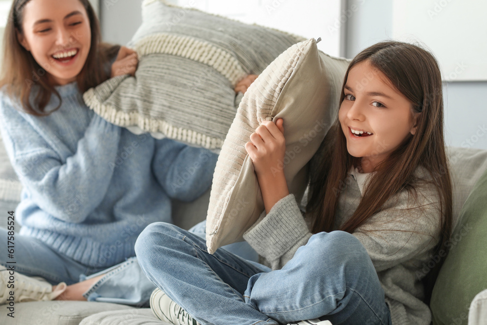 Little girl and her mother in warm sweaters fighting pillows at home