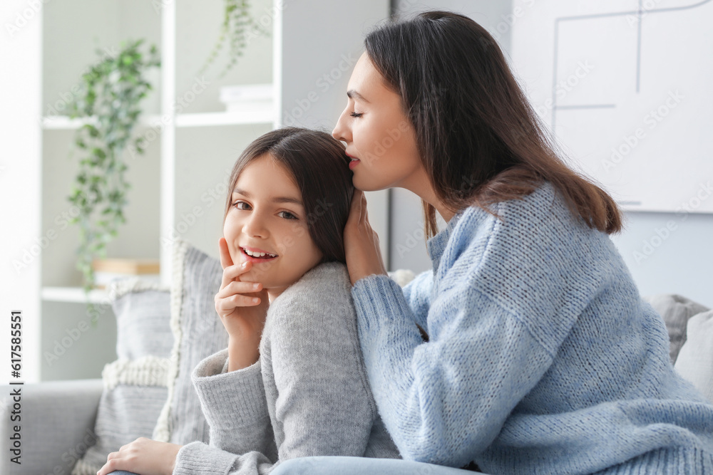 Little girl and her mother in knitted sweaters sitting on sofa at home