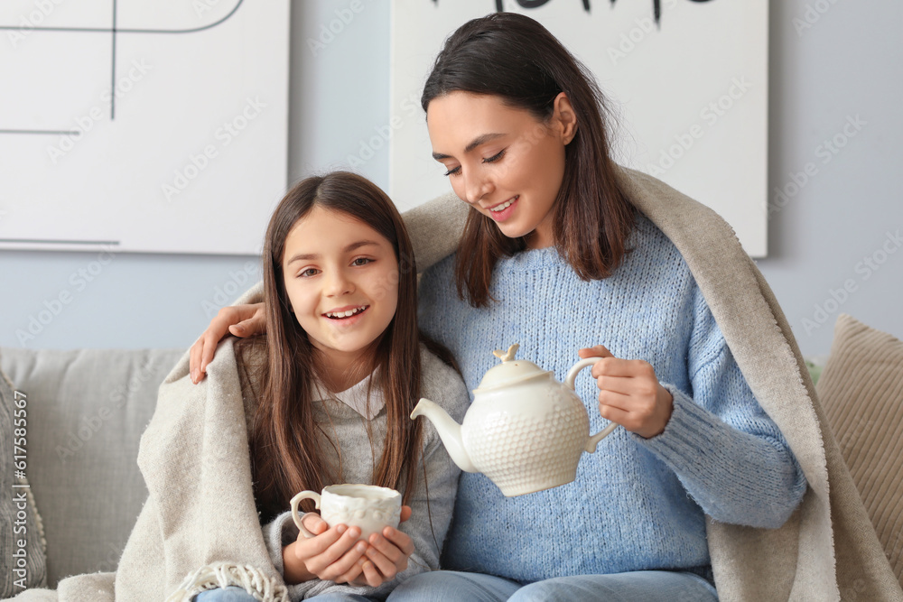 Mother pouring tea into her little daughters cup at home