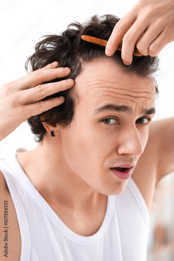 Upset young man with hair loss problem combing in bathroom, closeup