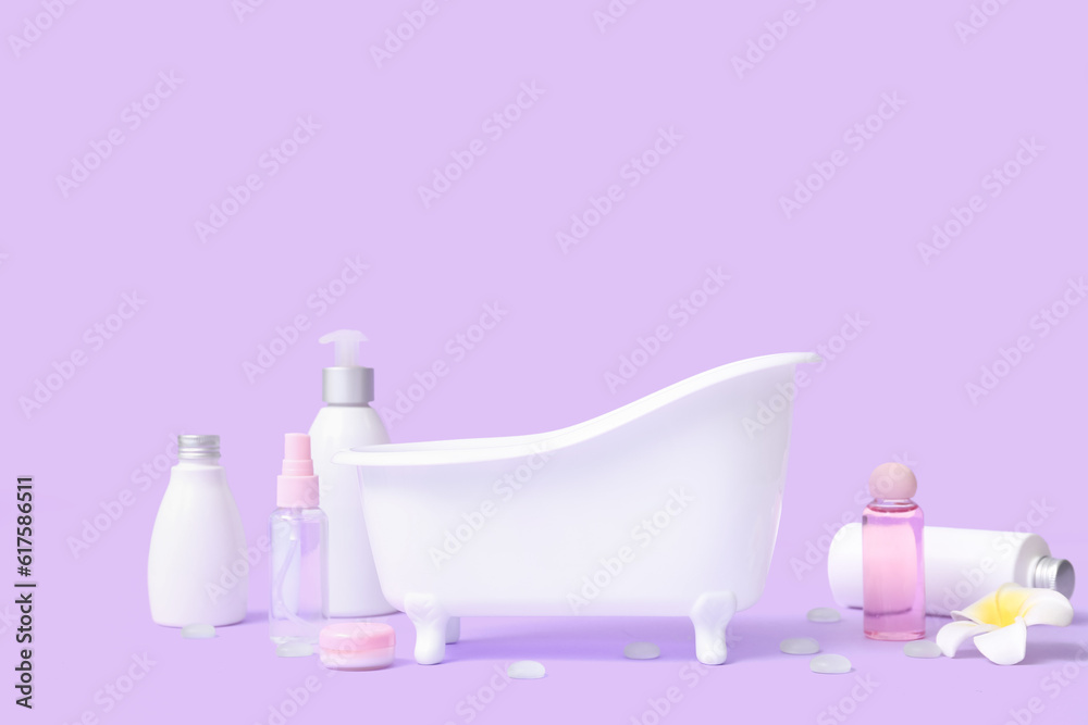 Small bathtub and cosmetic products on lilac background