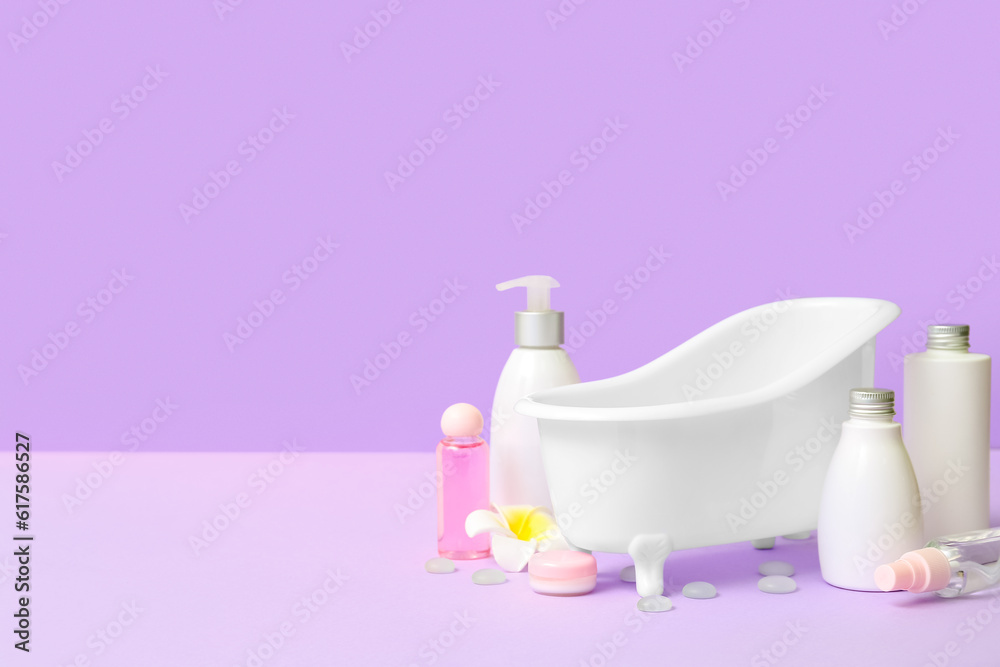 Small bathtub and cosmetic products on lilac background