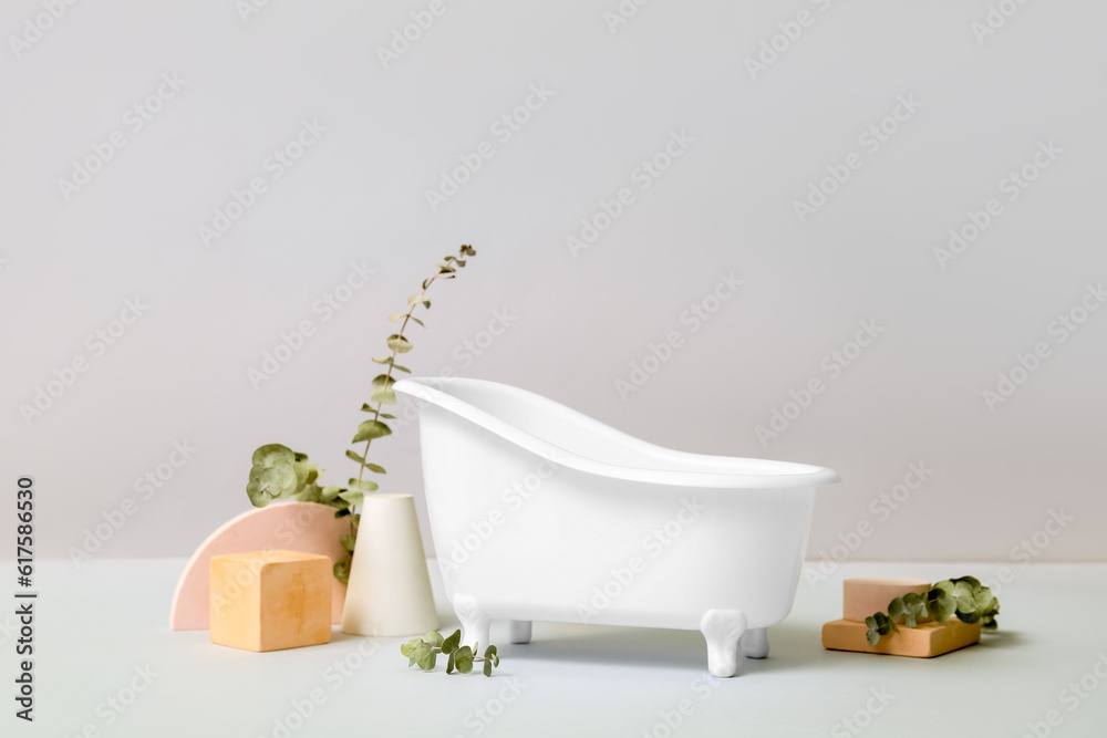 Small bathtub, plaster decor and eucalyptus branches on light background