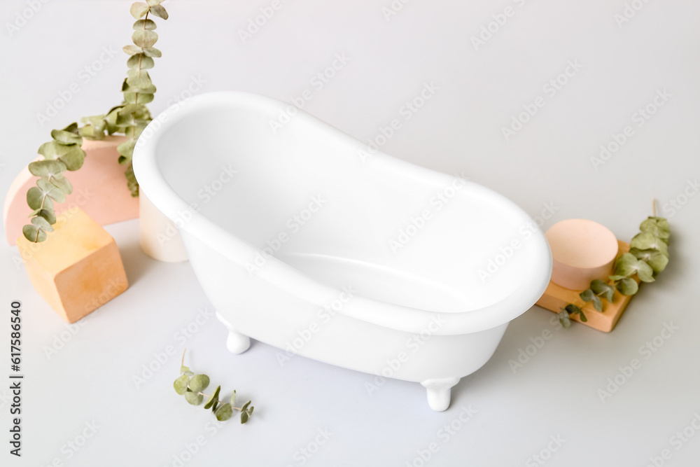 Small bathtub, plaster decor and eucalyptus branches on light background