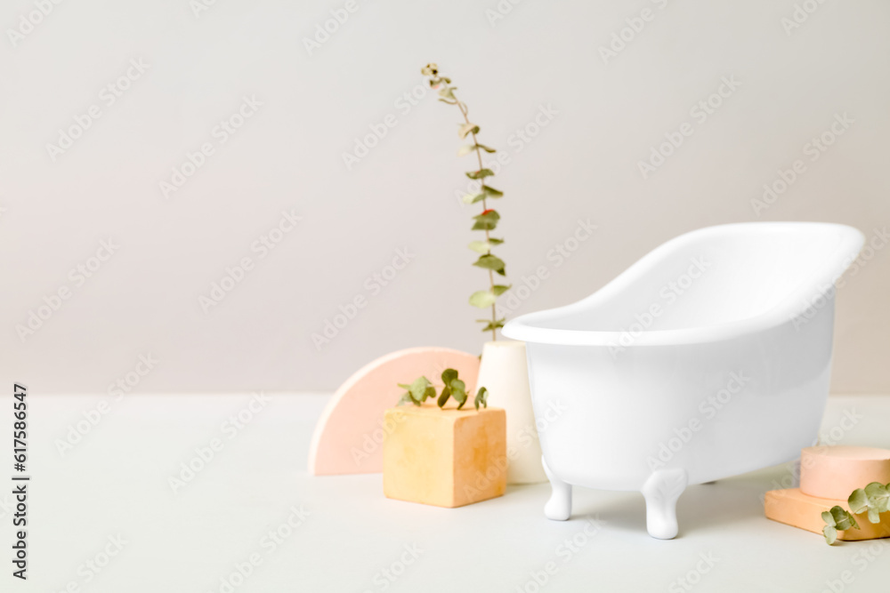 Small bathtub, plaster decor and eucalyptus branches on light background