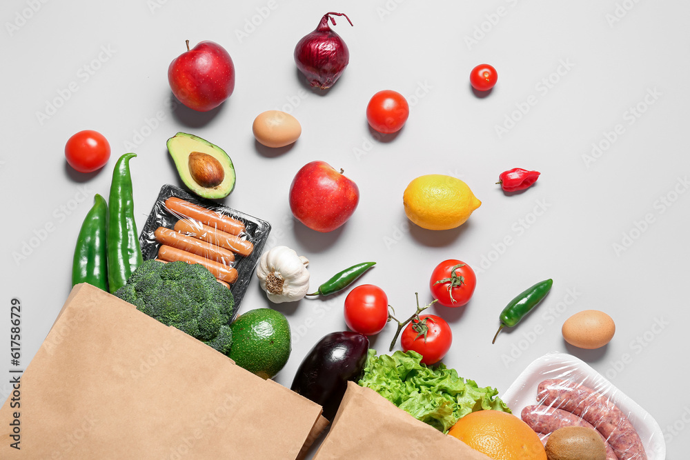 Paper bags with vegetables, fruits and sausages on grey background