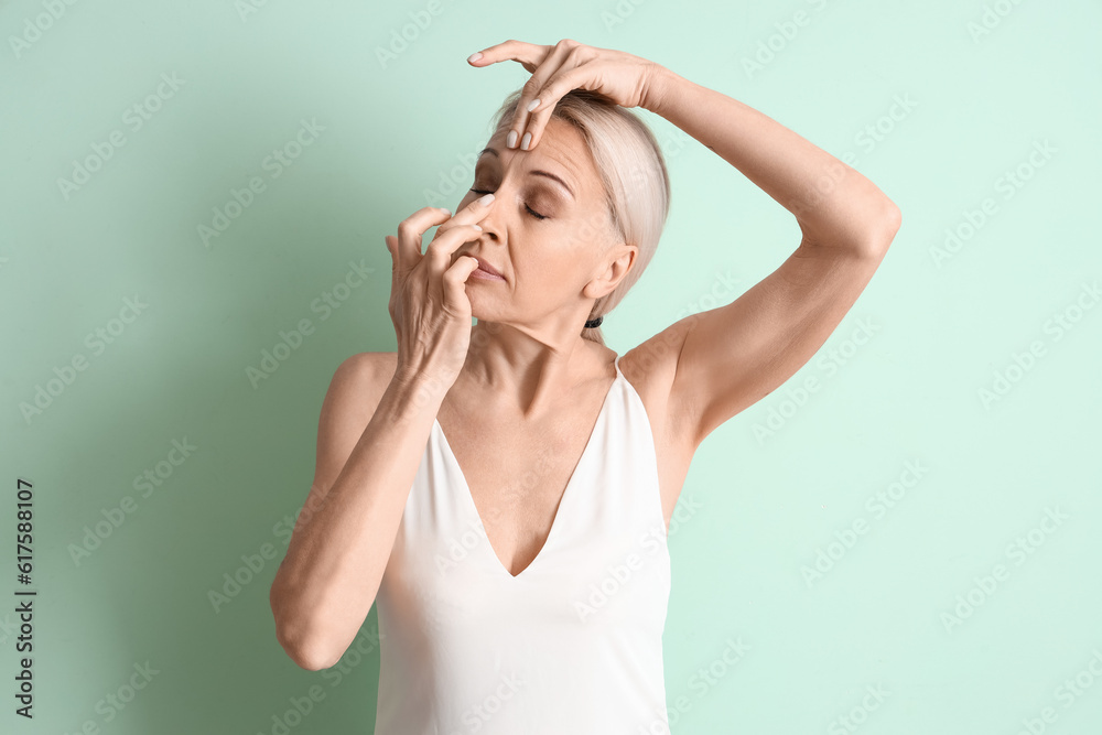 Mature woman doing face building exercise on green background