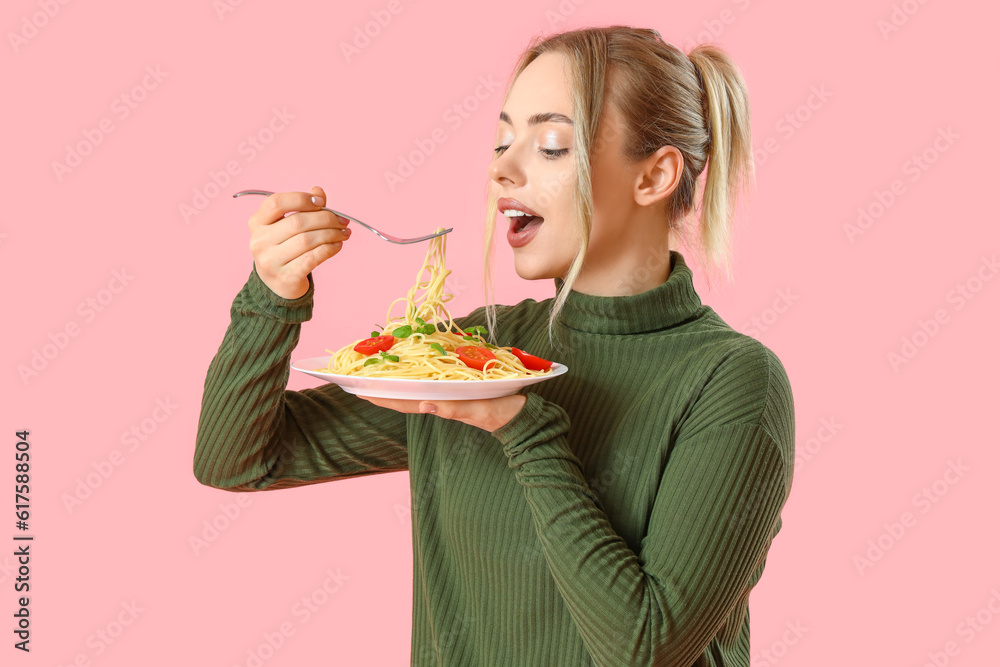 Young woman eating tasty pasta on pink background