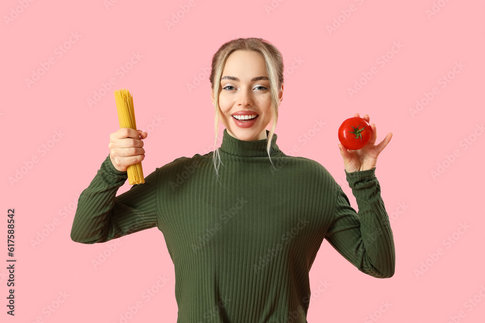 Young woman with raw pasta and tomato on pink background