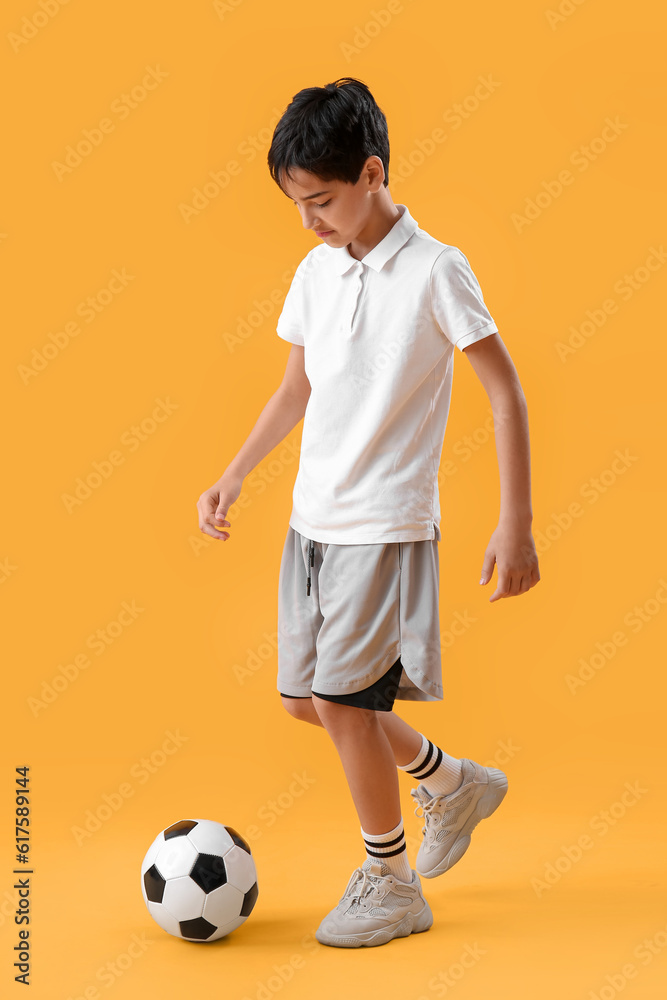 Little boy playing with soccer ball on yellow background