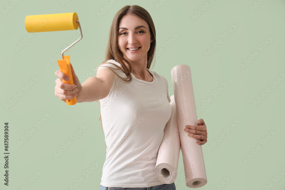 Young woman with wallpapers and roller on green background