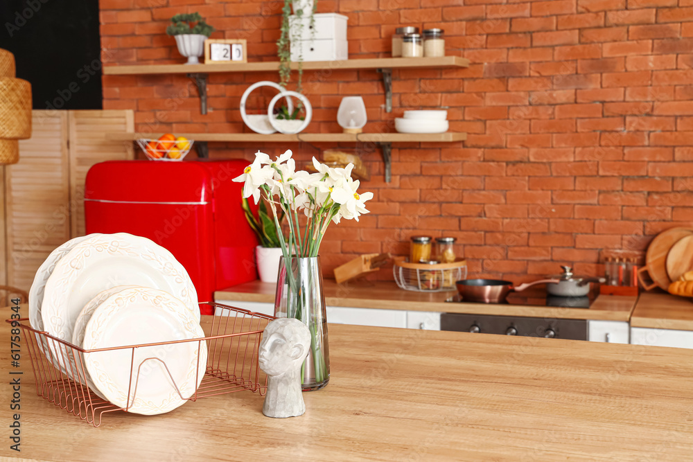 Vase with narcissus flowers and plates on table in interior of stylish kitchen, closeup