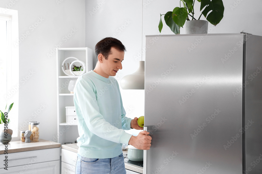 Handsome man opening fridge in kitchen