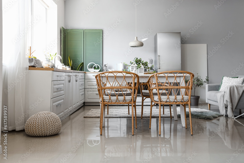 Interior of light kitchen with stylish fridge, counters, sofa, table and chairs