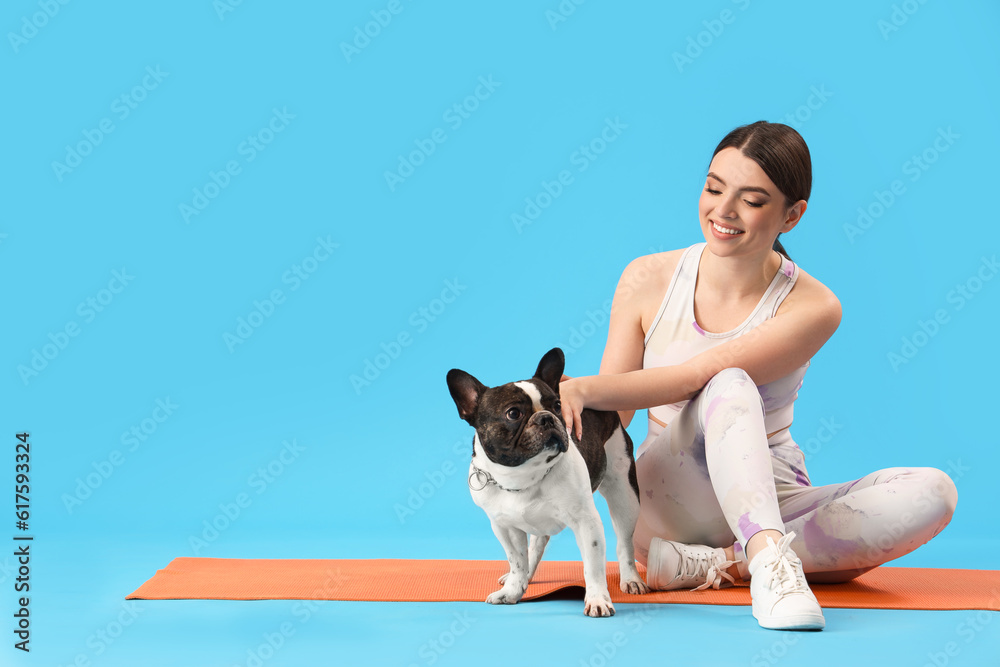 Sporty young woman with her French bulldog on blue background