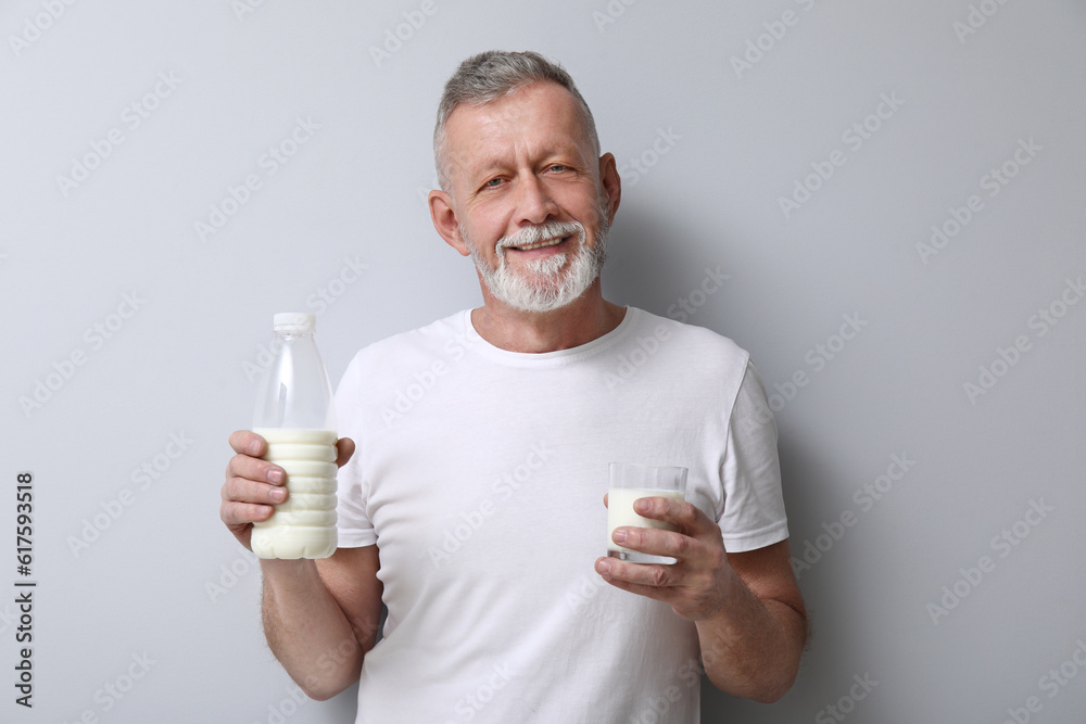 Mature man with bottle and glass of milk on light background