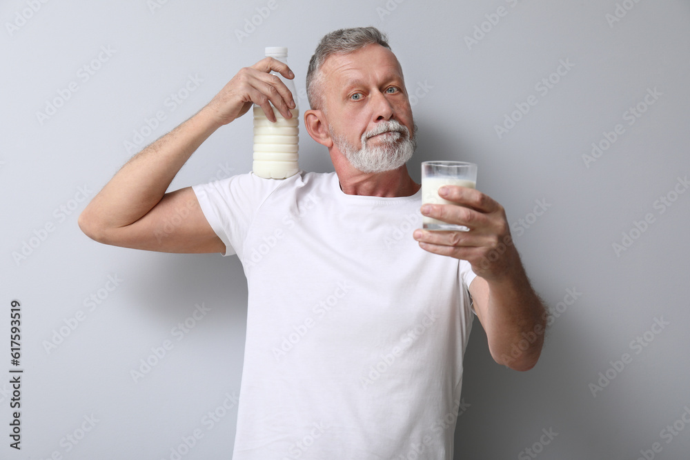 Mature man with bottle and glass of milk on light background