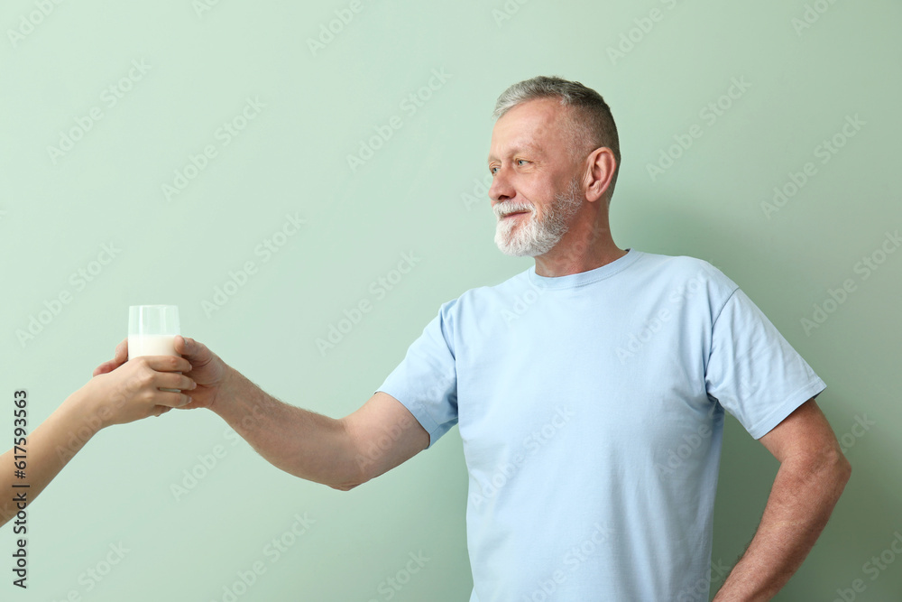 Mature man taking glass of milk on green background