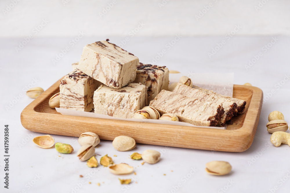 Wooden board with pieces of tasty marble halva on light background