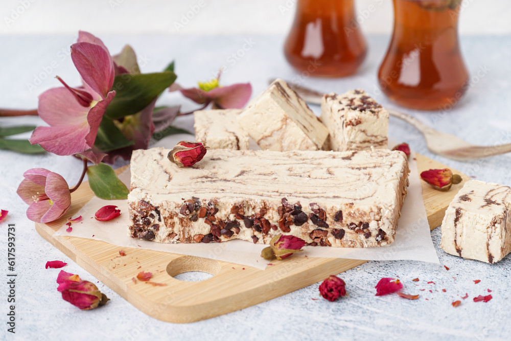 Wooden board with pieces of tasty marble halva on light background