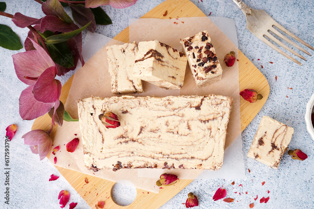 Wooden board with pieces of tasty marble halva on light background