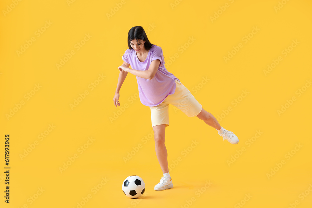 Young woman playing with soccer ball on yellow background