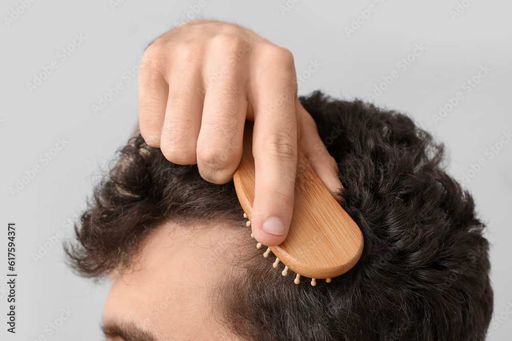 Young brunette man brushing hair on light background, closeup