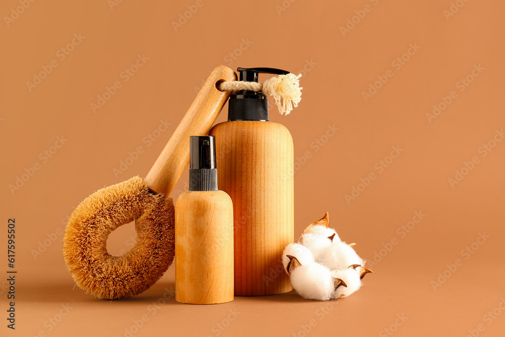 Bottles of cosmetic products, massage brush and cotton flowers on color background