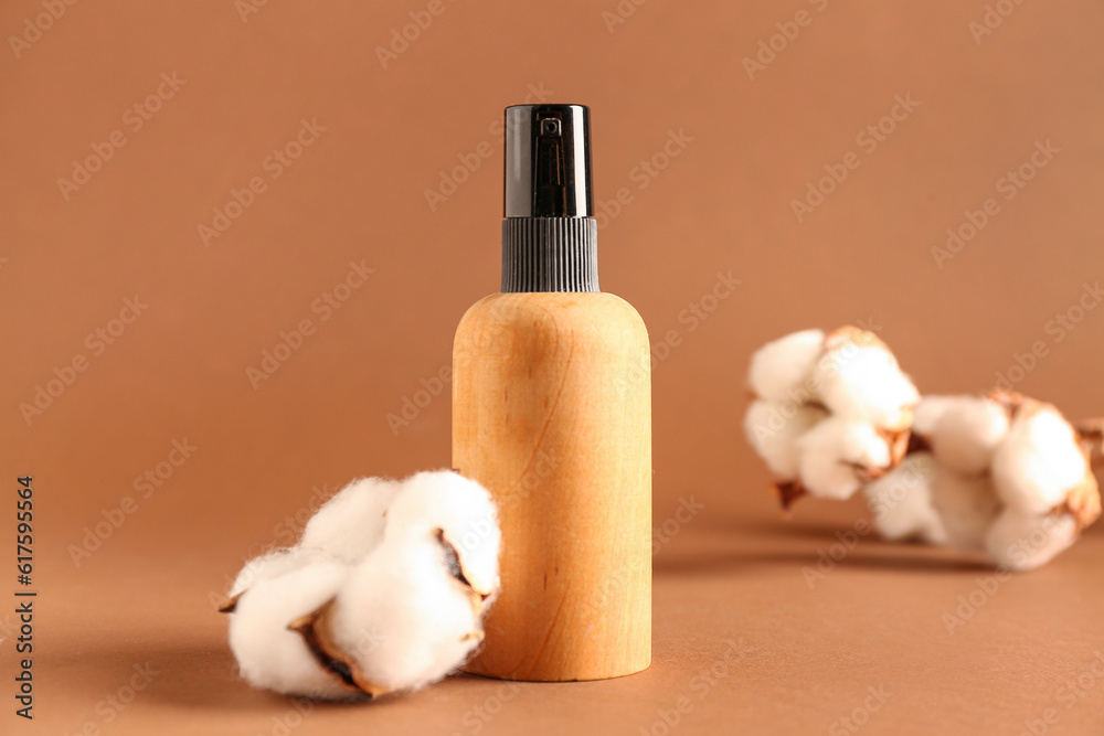 Bottle of cosmetic product and cotton flowers on color background