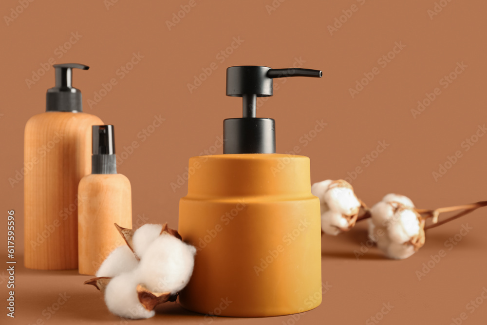 Bottles of cosmetic products with cotton flowers on color background