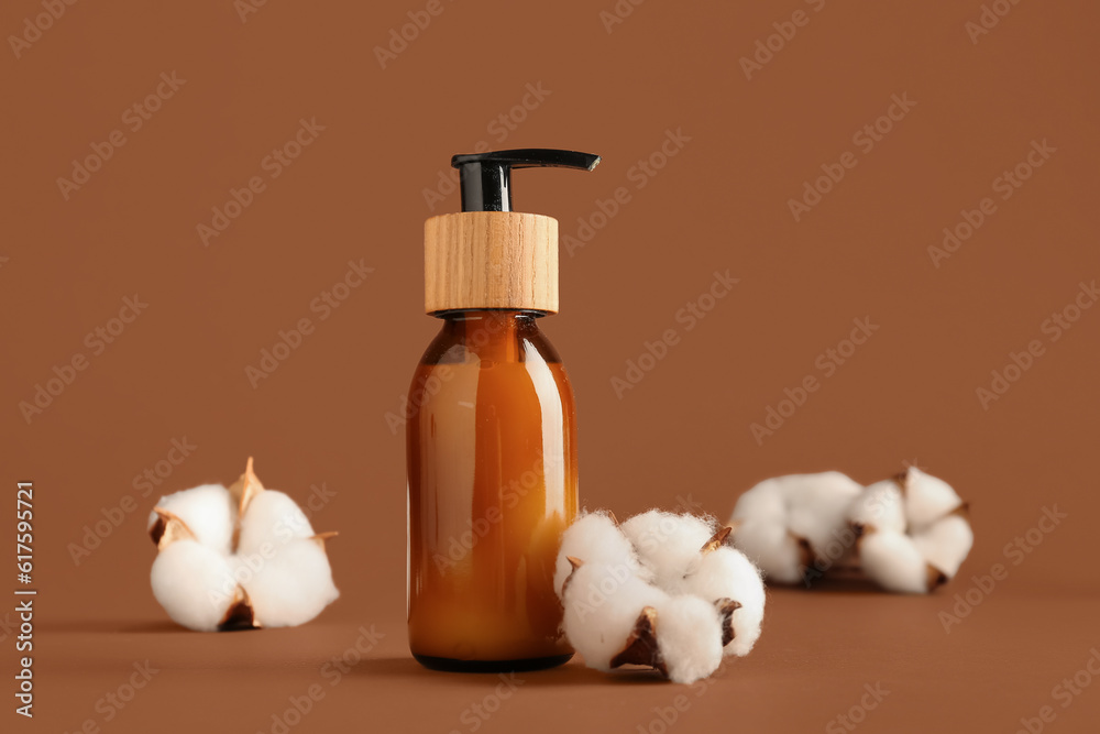 Bottle of cosmetic product and cotton flowers on color background