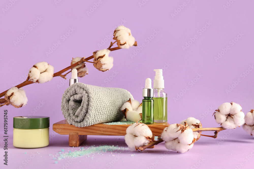 Composition with cosmetic products, clean towel and cotton branches on lilac background