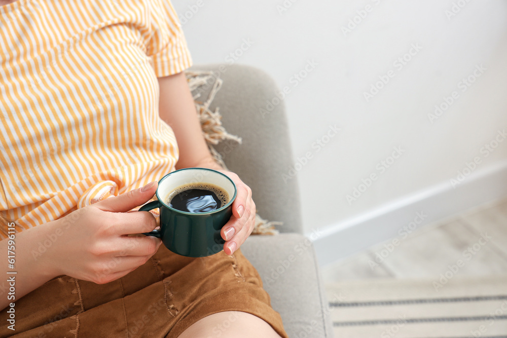 Woman sitting on cozy armchair and holding cup of delicious coffee