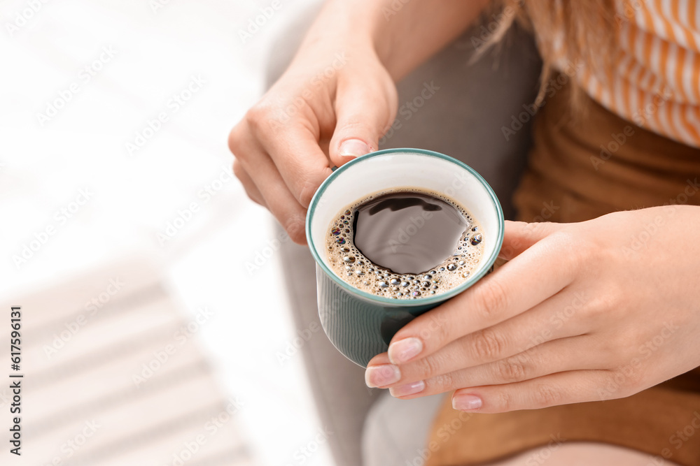 Woman sitting on cozy armchair and holding cup of delicious coffee