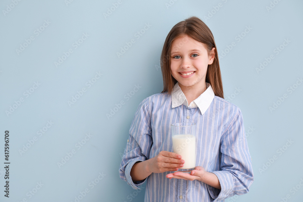 Little girl with glass of milk on light blue background