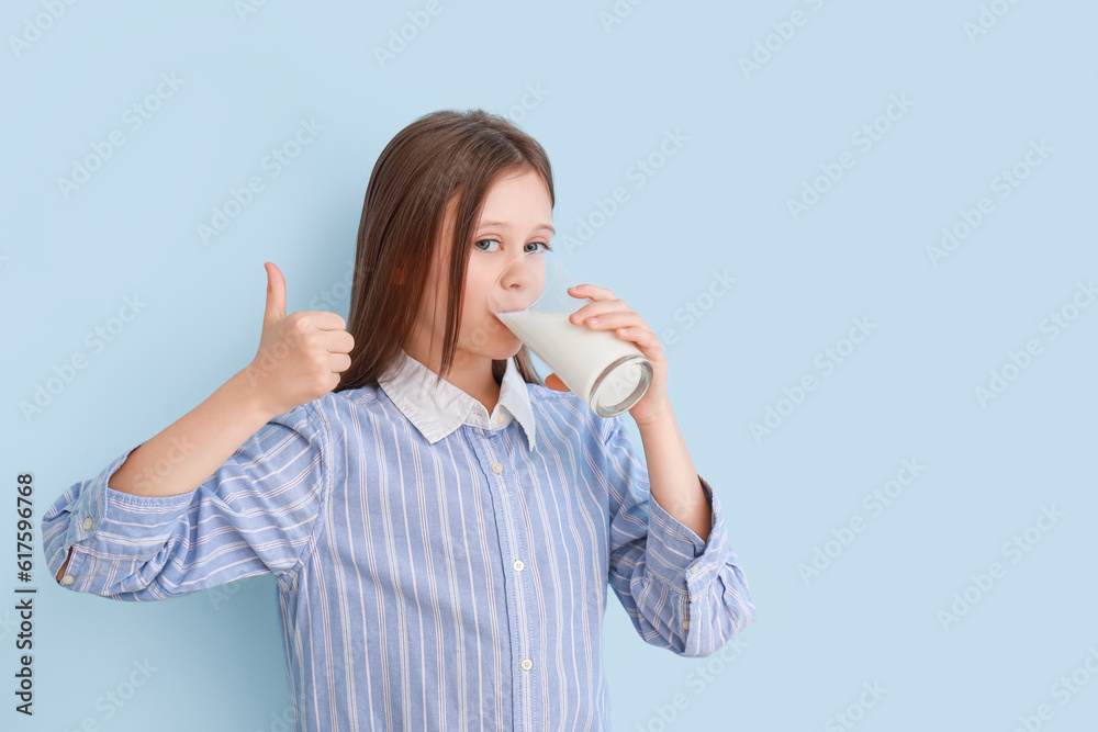 Little girl with glass of milk showing thumb-up on light blue background