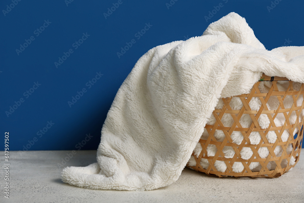 Basket with new soft blanket near blue wall, closeup