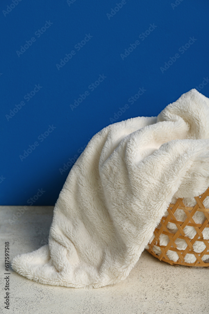 Basket with new soft blanket near blue wall