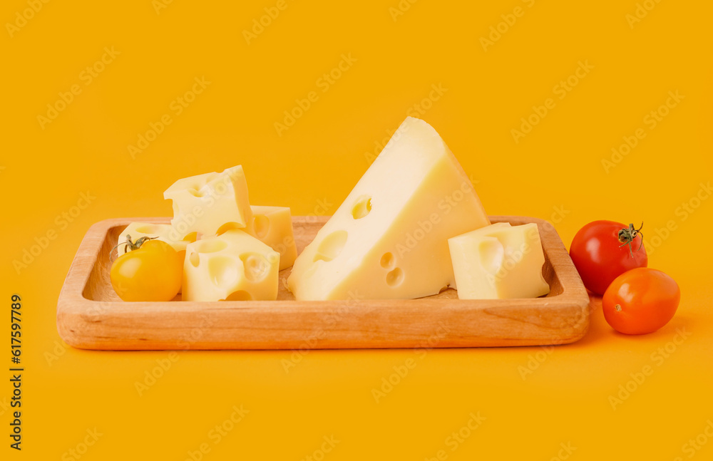 Board with pieces of Swiss cheese and tomatoes on orange background